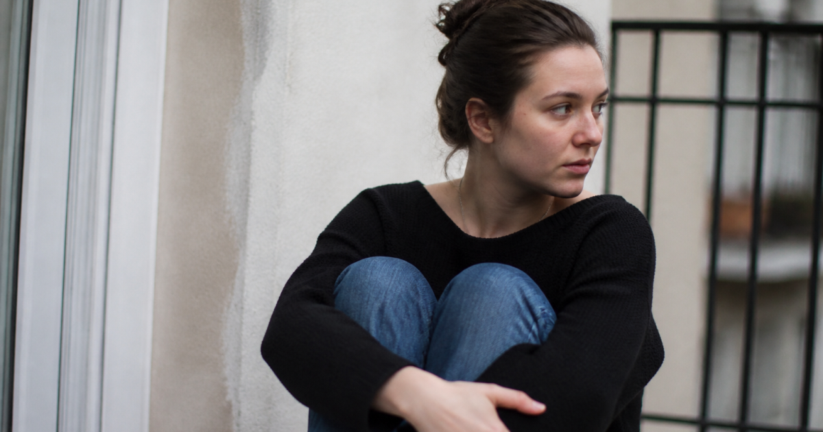 Femme assise seule, regard detourne, posture fermee et repliee.