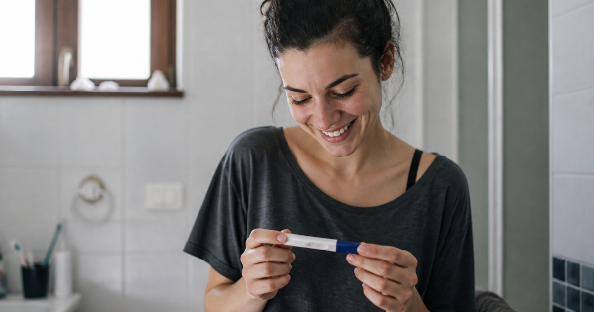 Femme tenant un test de grossesse positif, souriante