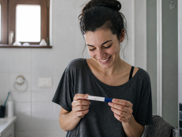 Femme tenant un test de grossesse positif, souriante