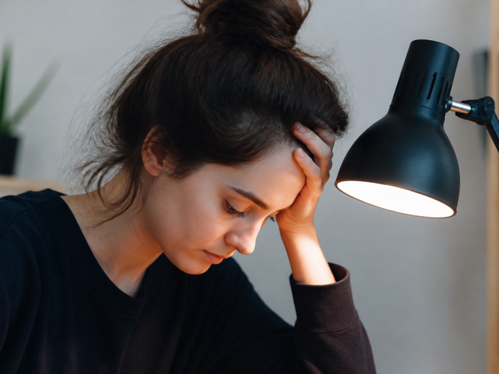 Femme tenant sa tete pres de la lampe de bureau.