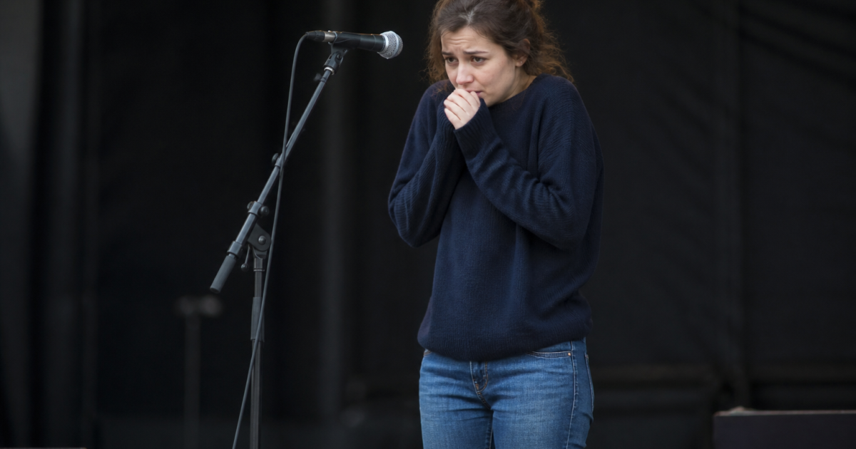 Femme tremblante devant microphone sur scene vide.