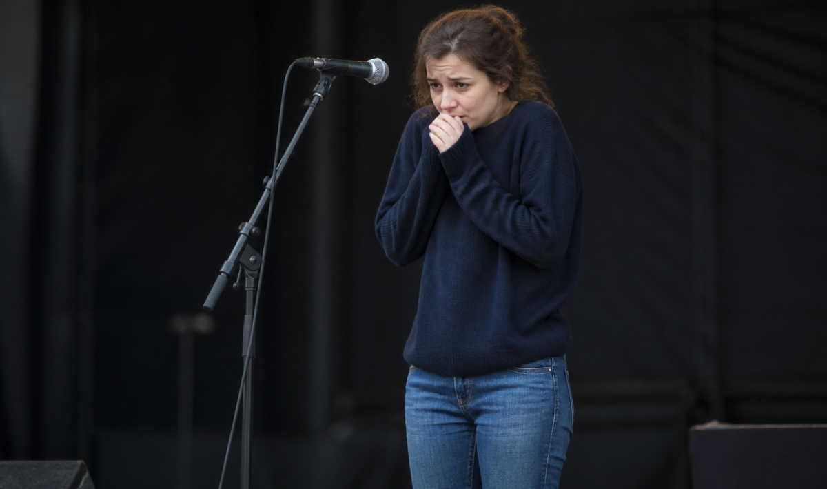 Femme tremblante devant microphone sur scene vide.