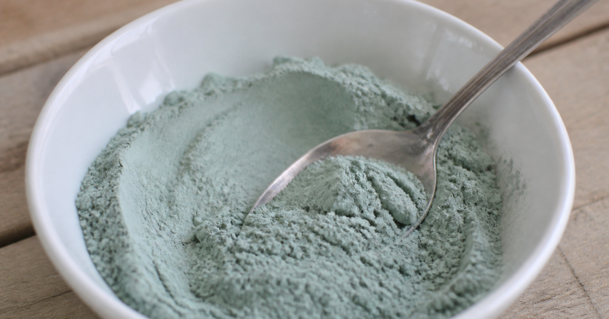 Poudre bleue-verte dans bol blanc avec cuillere.
