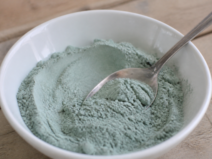 Poudre bleue-verte dans bol blanc avec cuillere.