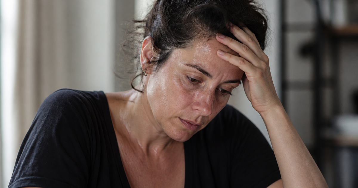 Femme tenant sa tête, regard fatigué, sueurs visibles