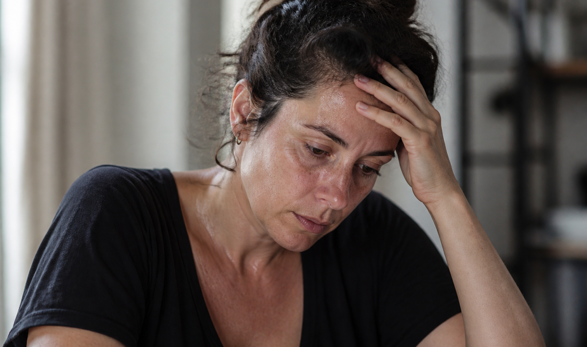 Femme tenant sa tête, regard fatigué, sueurs visibles