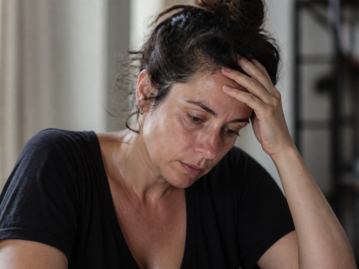 Femme tenant sa tête, regard fatigué, sueurs visibles