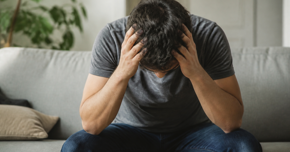 Homme assis penche en avant tenant sa tete fatigue
