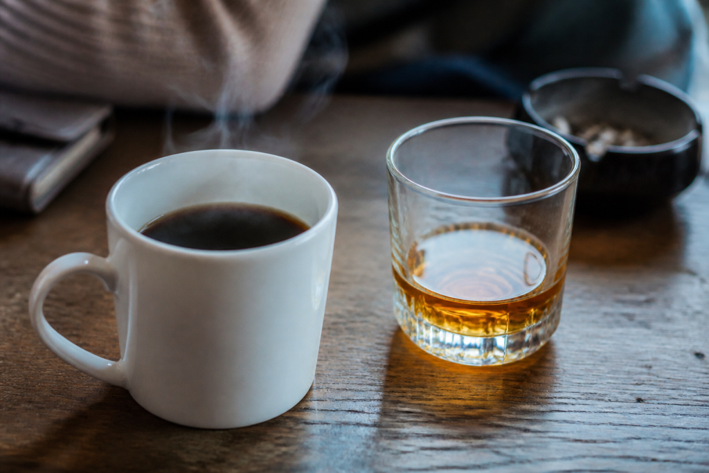 Tasse de cafe noir fumante pres d'un verre d'alcool