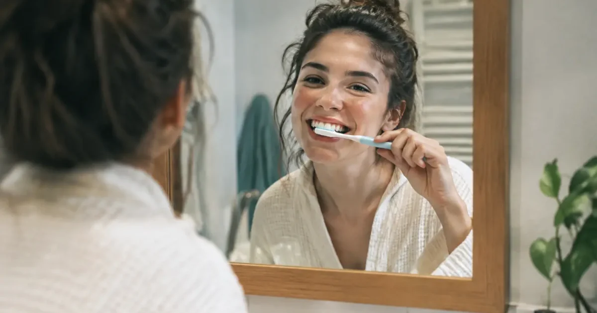 Femme souriante brossant ses dents devant le miroir