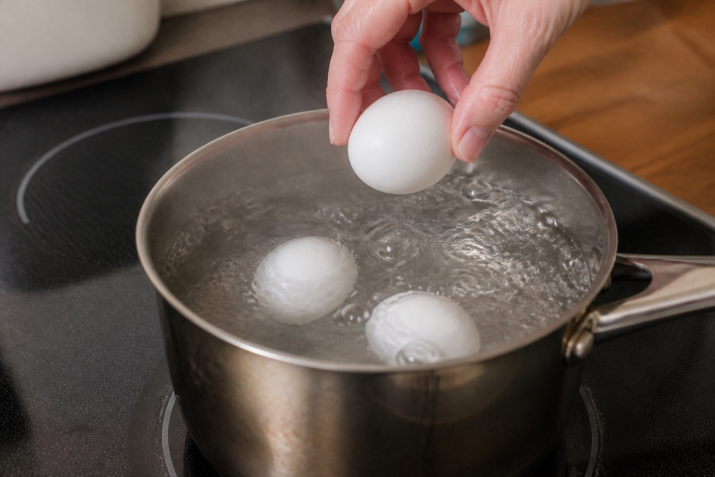 Trois oeufs blancs plongent dans une casserole bouillante